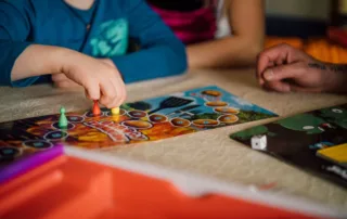 Fotografia przedstawia kadr dłoni dzieci grających w gry planszowe